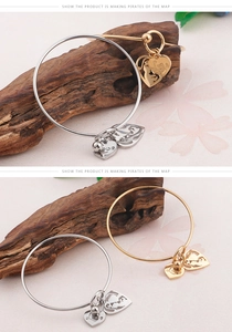 Close-up of gold and silver steel bangles with heart charms on wooden display