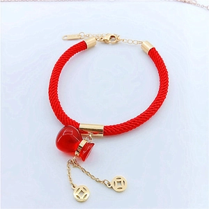 Detail of red braided lucky cord bracelet with gold coins and calabash charm