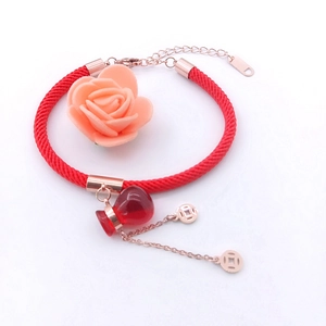 Macro view of a red woven rope bracelet with rose gold clasp and lucky pendant
