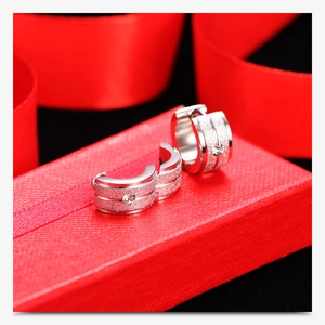 Macro detail of silver frosted huggie earrings with round diamond on red silk ribbon