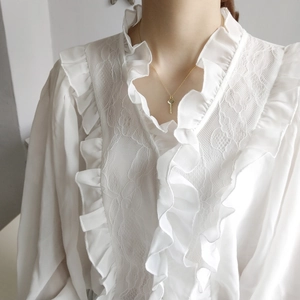 Close-up of a minimalist gold key pendant necklace worn on a white lace collar