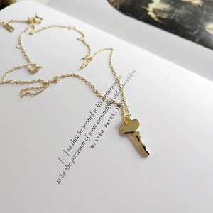 Close-up of 925 sterling silver gold key necklace resting on an open vintage book page