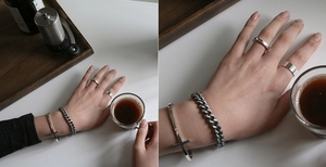 Silver jewelry set including cross cuff, cuban chain bracelet, and minimalist rings on hand