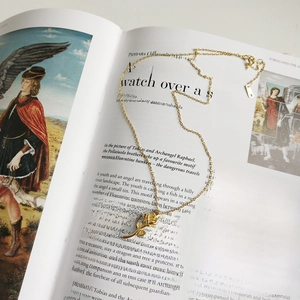 Artistic detail of a rose pendant necklace in gold finish over a vintage art book background