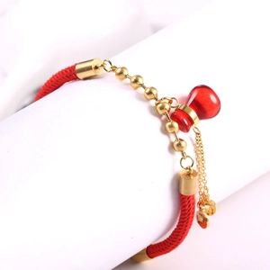 Vue macro d'un bracelet en corde tressée rouge avec perles dorées et petit pendentif