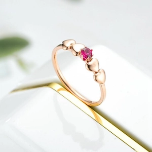 Close-up of rose gold titanium ring featuring a red zircon stone and heart patterns