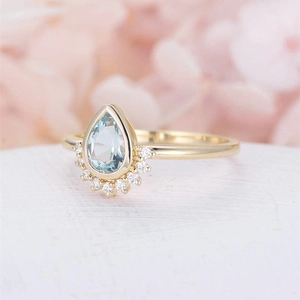 Elegant gold ring with pear-shaped blue gemstone and crown-style diamond setting