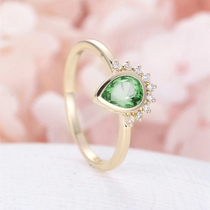 Elegant gold pear-cut green gemstone ring with white zircon accents on floral background