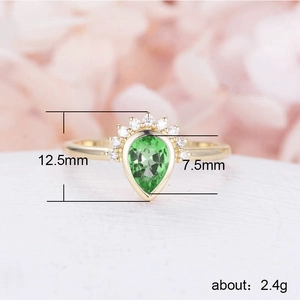 Elegant gold pear-shaped green zircon ring with crown-set diamonds on white surface