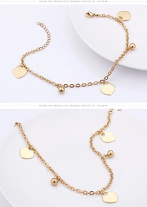 Detailed view of golden anklet with flat heart charms and polished beads on white ceramic