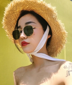 Detailed close-up of golden metal frame sunglasses with green lenses and raffia hat