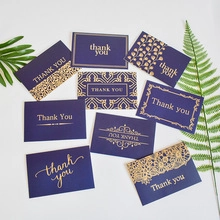Flat lay of navy blue cards with gold foil thank you text and green leaf decoration