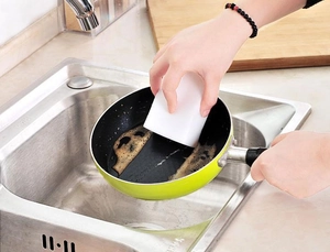 Close-up of hands using a white nano magic sponge to scrub stains off a green frying pan