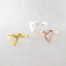 Macro detail of minimalist geometric triangle rings in gold, silver, and rose gold finishes