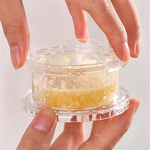 Manual plastic garlic press and mincer in use showing crushed garlic inside container