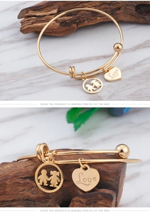 Detail of gold LOVE heart pendant and boy girl silhouette charm on titanium steel bangle