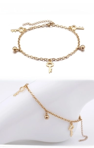 Detail of gold key anklet showing polished charms and extension chain on foot