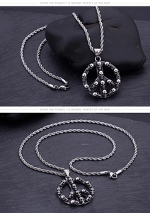 Detailed macro view of a silver skull peace sign pendant with a twisted chain on black stone