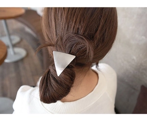 Detail of a silver triangular metal hair tie worn on a ponytail in a chic cafe setting