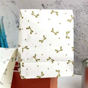 Detail of white paper gift bag featuring elegant gold bow and dot patterns for party favors