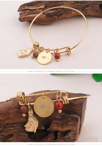 Detailed close-up of golden open bangle with I Love You charm and red gemstone beads