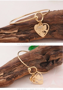 Macro detail of gold love heart charm bangle with hollow mother and child silhouette