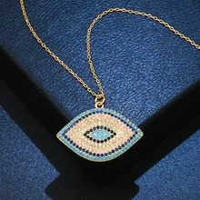 Close-up of golden evil eye necklace with blue and white zircons on blue fabric