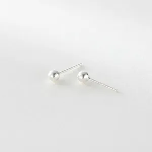 Macro shot of minimalist sterling silver ball stud earrings on a textured white surface