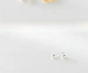 Macro shot of minimalist sterling silver ball stud earrings on a textured white surface