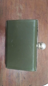 Close-up of a green hard-shell evening clutch bag with a silver pearl clasp on wood