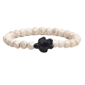 Macro detail of white marble stone beads and a black turtle charm on a stretch bracelet
