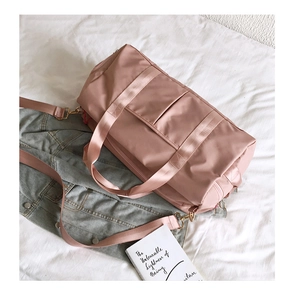 Pink fitness duffel bag with gold metal buckles and adjustable strap on a bed