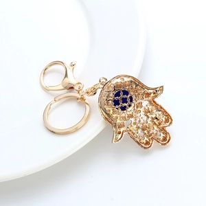 Detail view of golden Hamsa hand keychain with blue clover center on a white plate