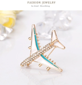 Close-up of golden airplane brooch with sparkling rhinestones and white enamel finish