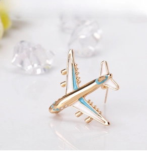 Detailed close-up of a gold airplane brooch with blue and white enamel on a white surface
