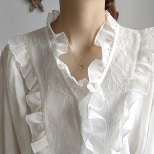 Close-up of golden key pendant necklace worn with an elegant white lace blouse