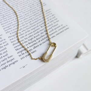 Detailed close-up of a golden safety pin necklace with pavé zircons on an open book