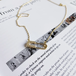 Detail shot of a gold safety pin pendant necklace with pave crystals on a book page