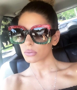 Detail of square glitter sunglasses with red and green gradient frame and dark lenses