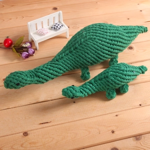 Detail of green dinosaur cotton rope dog chew toy on a textured wooden surface