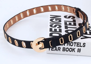 Detail of black faux leather belt with metal eyelets and a round gold buckle on a white book