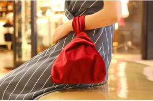Detail of red velvet Japanese knot wrist bag held by model in striped dress