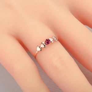Close-up of rose gold ring with heart patterns and a central red zircon on a finger
