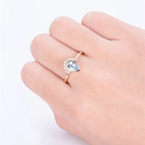 Rose gold pear shaped ring with light blue zircon and crown-set diamonds on model hand