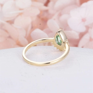 Macro shot of a pear-cut green gemstone ring with a polished gold band on floral decor