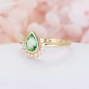 Macro shot of gold ring with pear-cut green gemstone and crown-shaped diamond halo