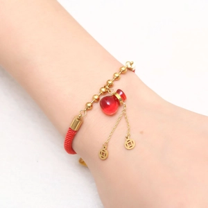 Bracelet tressé rouge avec breloque gourde en or rose et pièces porté au poignet femme
