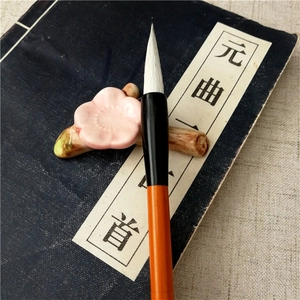 Macro view of a ceramic plum blossom pen rest with a bamboo calligraphy brush on vintage paper
