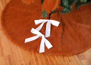 Close-up of brown plush Christmas tree skirt with two white ribbon bows on wood floor