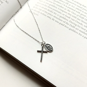 Vintage 925 sterling silver cross and virgin mary necklace on an open book background